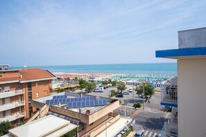 A coastal view with a beach, buildings, and solar panels on a rooftop. - Hotel Alexander (Riccione)