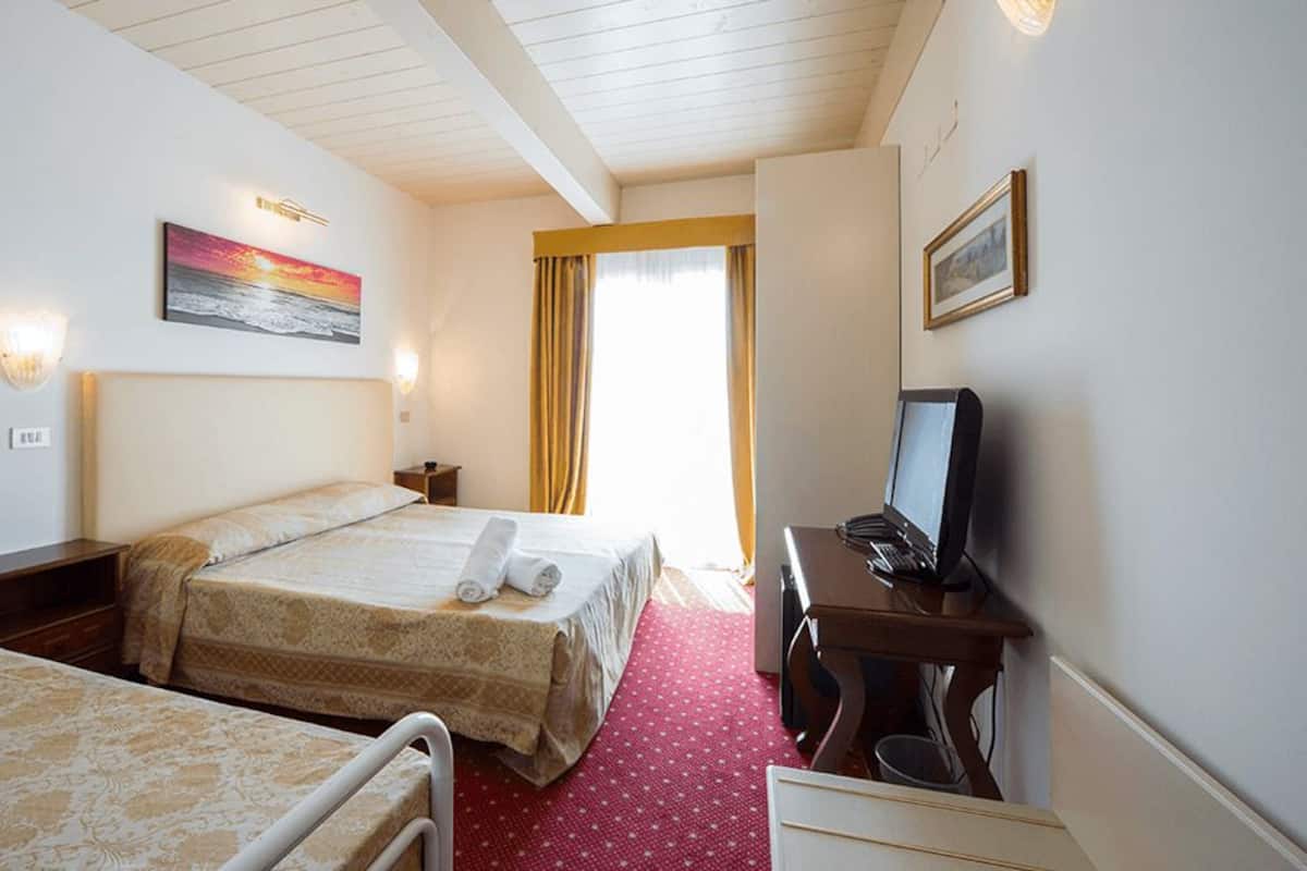A hotel room with two beds, a desk, a chair, a television, and a window with curtains.