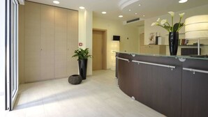 A modern reception area with a glass counter, a potted plant, and a large mirror reflecting the interior. - Residence Hotel Rubino (Riccione)