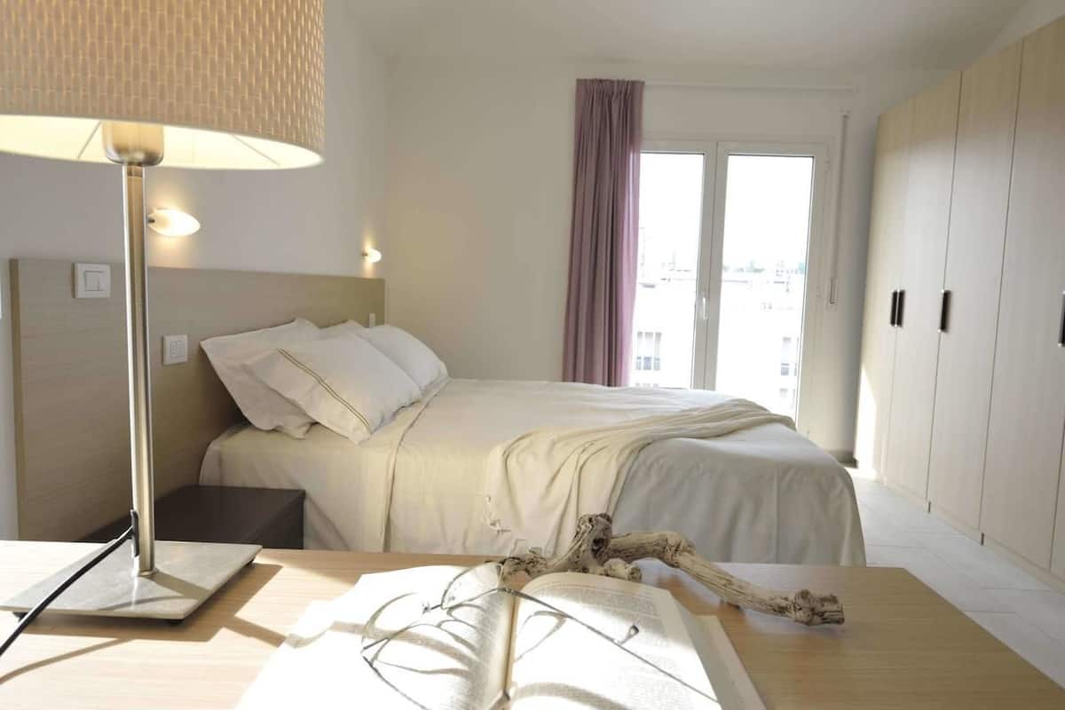 Quarto de hotel com cama, luminária de cabeceira e vista para a cidade pela janela.