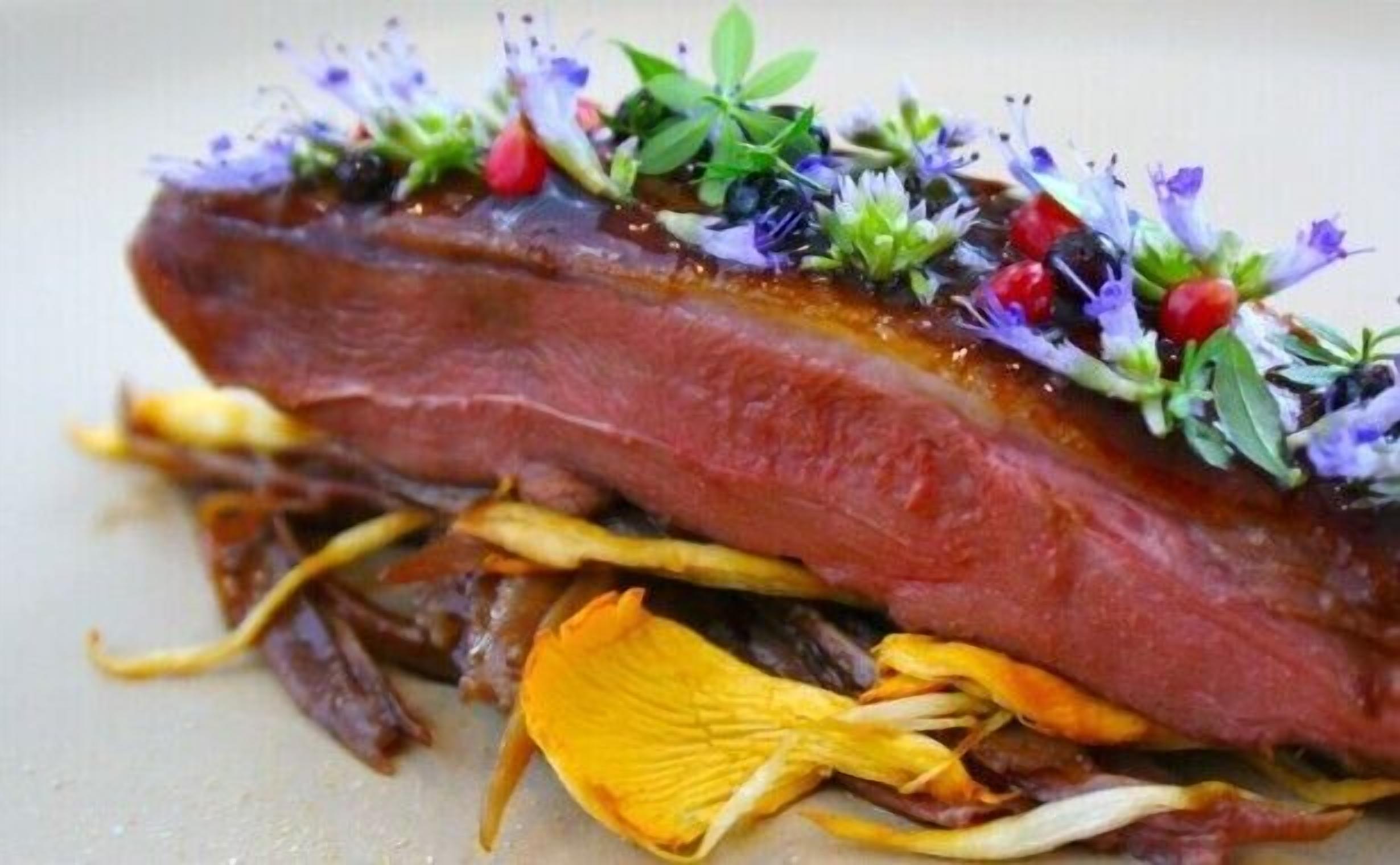 A dish with a piece of meat, possibly duck, garnished with flowers and herbs.