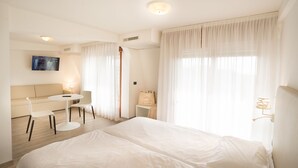 A hotel room with a bed, a sofa, a small table, and a TV. - Fantinello Hotel (Caorle)