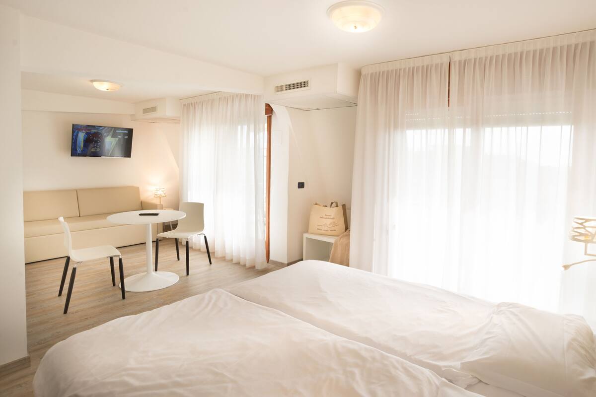 A hotel room with a bed, a sofa, a small table, and a TV.