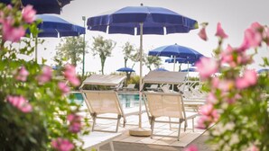 A poolside area with lounge chairs and blue umbrellas. - Fantinello Hotel (Caorle)