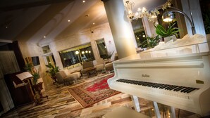 A grand piano in a spacious lobby with a patterned floor, comfortable seating, and decorative plants. - Fantinello Hotel (Caorle)
