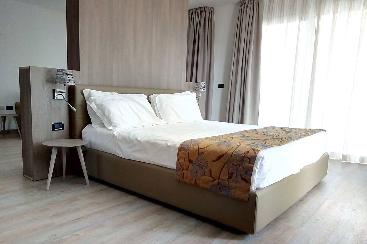 A modern hotel room with a large bed, a small side table, and a wooden nightstand.