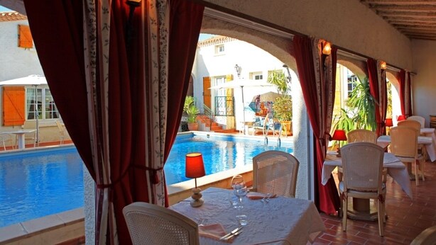 A dining area with a pool view, featuring a table set for two, wicker chairs, and red curtains.