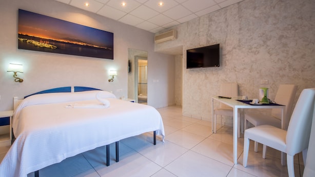 A hotel room with a bed, a desk, a chair, a TV, and a painting on the wall. - Casa Matilde (Sorrento)