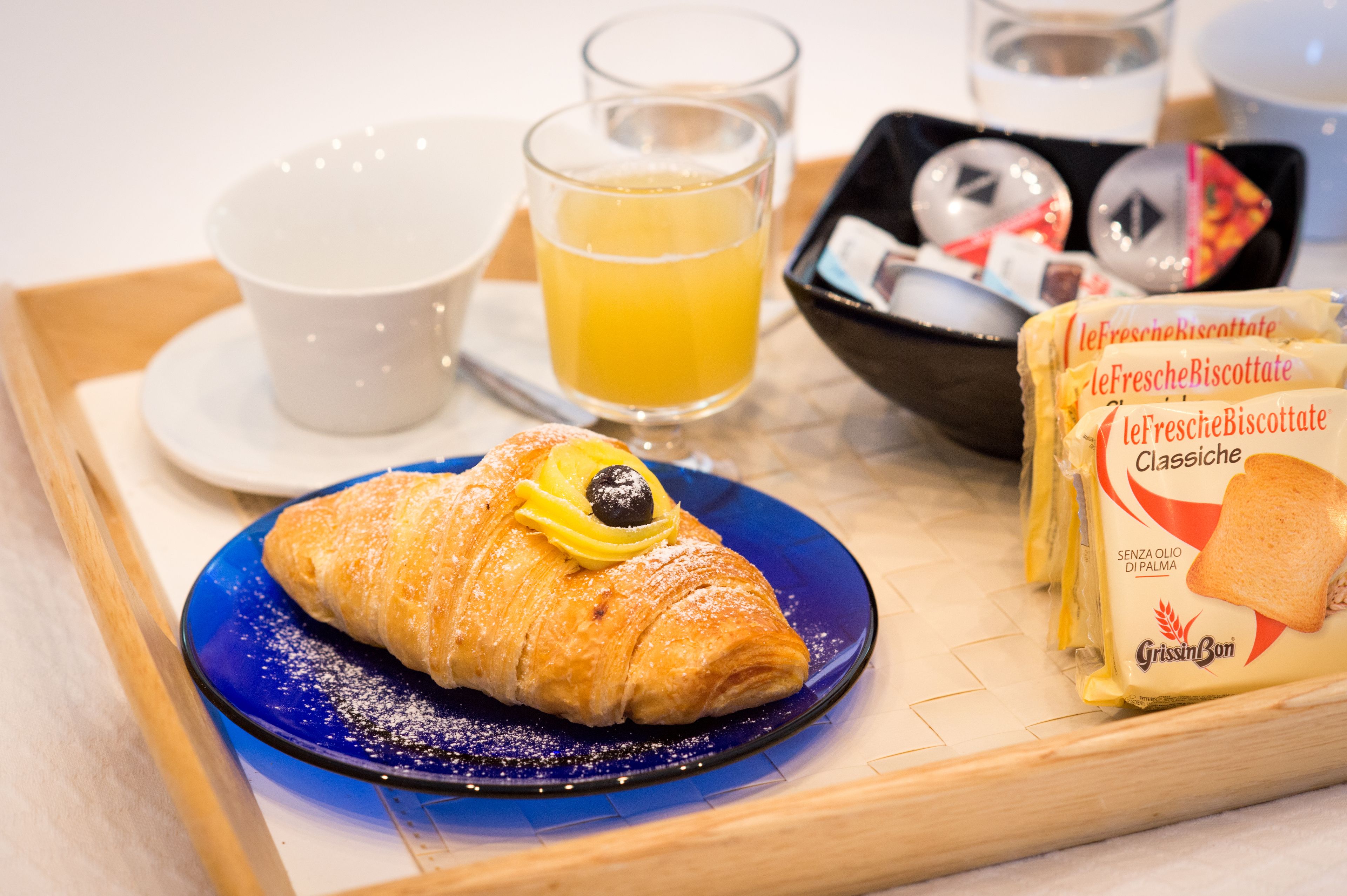 A breakfast tray with a croissant, a glass of orange juice, a bowl of biscotti, and a cup.