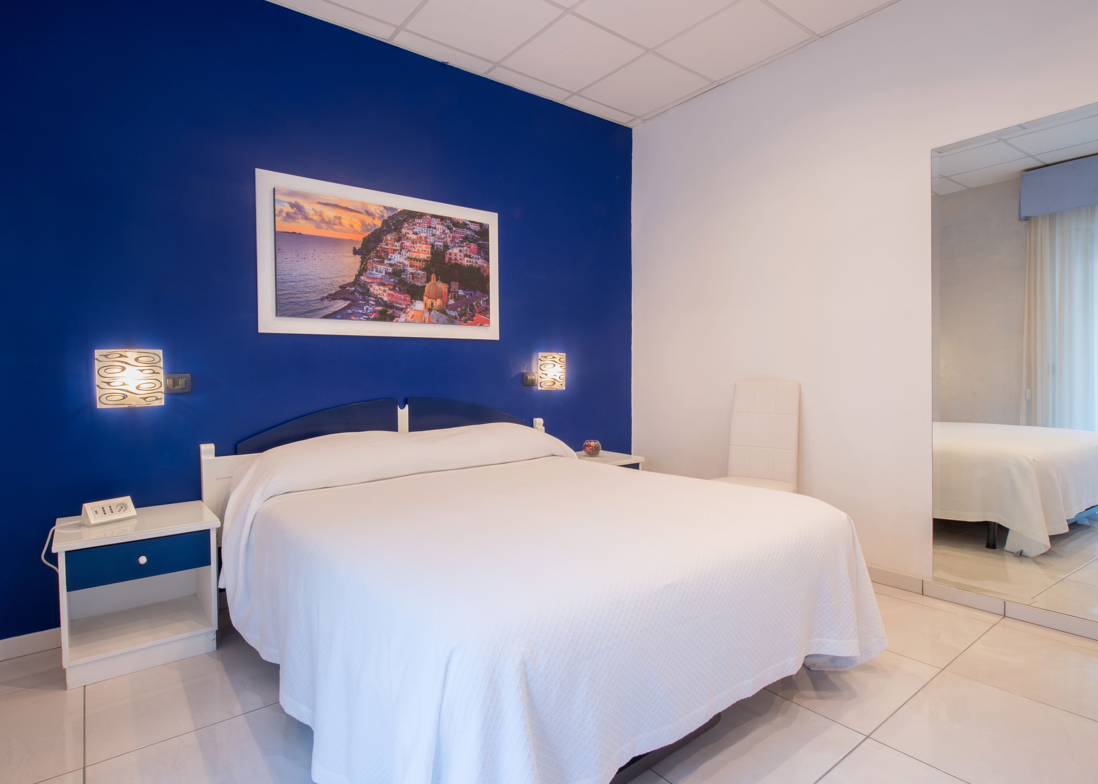 A hotel room with a large bed, a nightstand, a bedside table, and a wall-mounted picture.