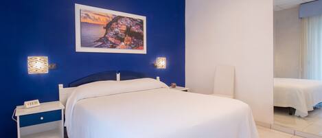 A hotel room with a large bed, a nightstand, a bedside table, and a wall-mounted picture.