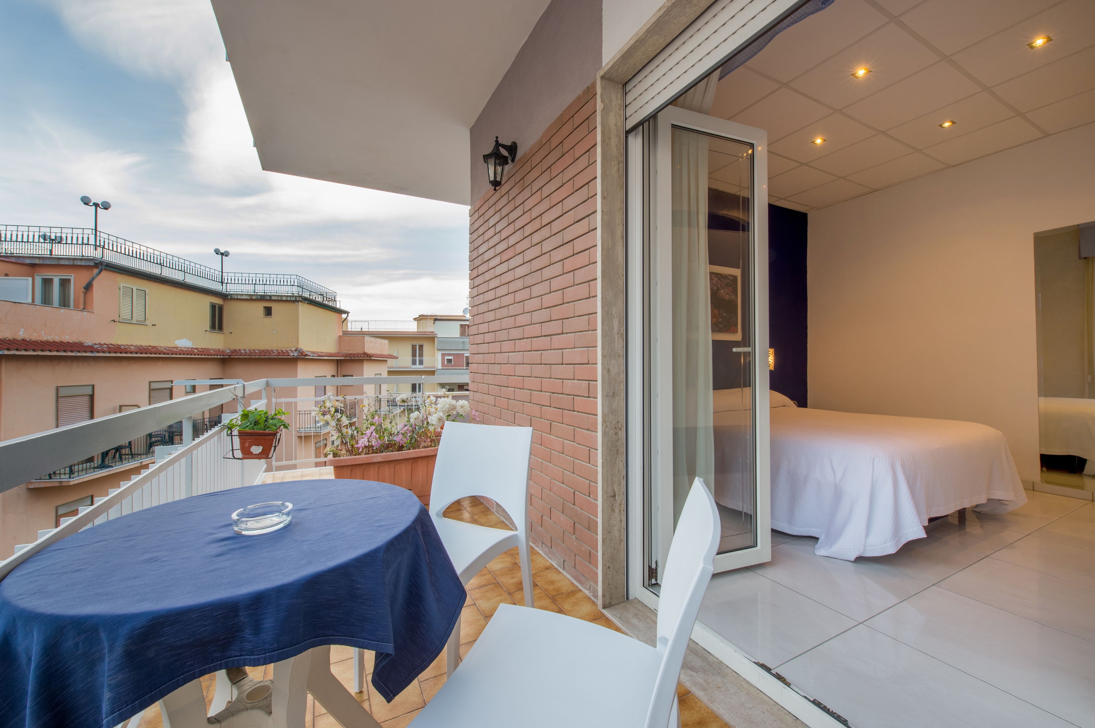 Un balcón con mesa y sillas, una cama y vistas de edificios cercanos.