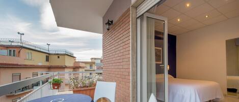 Un balcón con mesa y sillas, una cama y vistas de edificios cercanos.