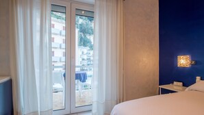 A hotel room with a bed, a nightstand, a wall-mounted light, and a sliding glass door leading to an outdoor area with a table and chairs. - Casa Matilde (Sorrento)
