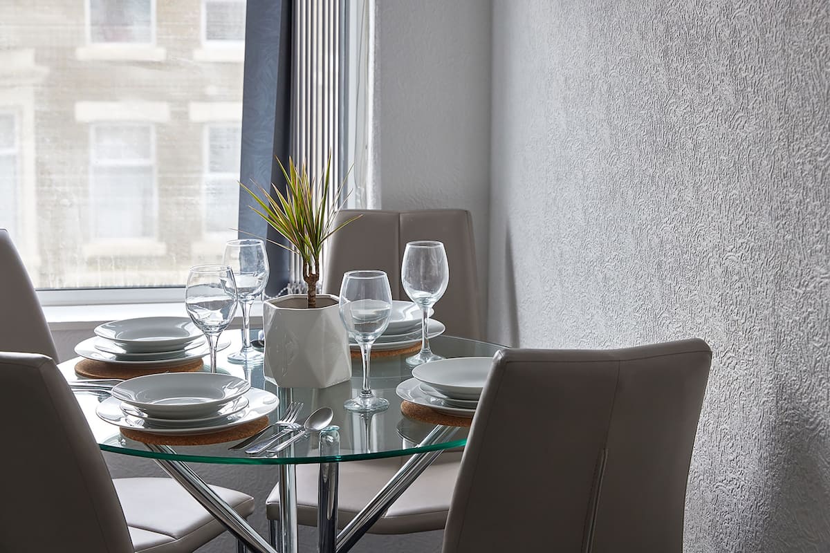 A dining table set with plates, glasses, and cutlery, with a plant and a vase on the table.