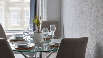A dining table set with plates, glasses, and cutlery, with a plant and a vase on the table.