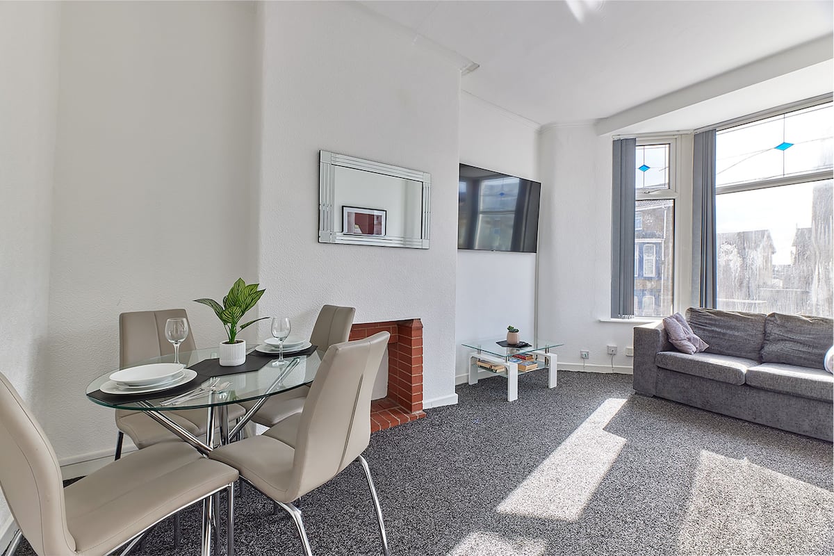 A modern living room with a glass dining table, a sofa, and a fireplace.