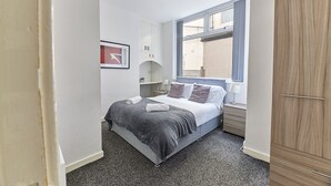 Habitación de hotel pequeña con cama, armario, ventana y mesita de noche.
