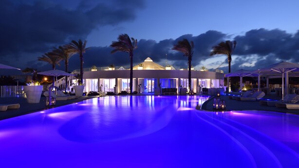 A pool area with lounge chairs and umbrellas, palm trees, and a building with a dome roof. - Soleinme Resort (Ostuni)