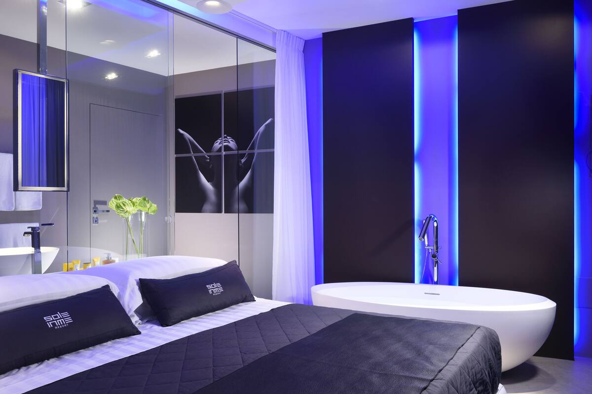 Une chambre à coucher moderne avec un grand lit, une baignoire blanche et une douche séparée par des parois en verre.