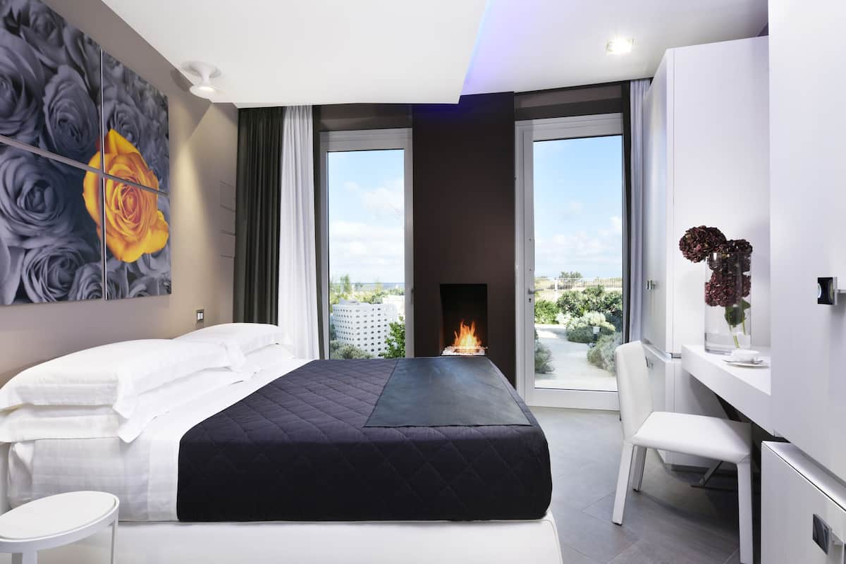 Une chambre moderne avec un grand lit, un bureau et une vue sur le paysage urbain, grâce à de grandes fenêtres.