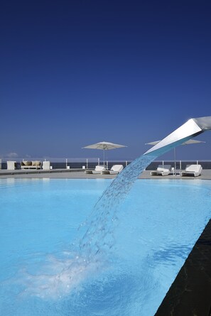 Ein Pool, in den Wasser fließt, umgeben von Liegestühlen und Sonnenschirmen.