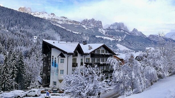 A hotel with a traditional Alpine architectural style, surrounded by snow-covered trees and mountains.
