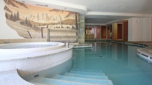 A swimming pool with a hot tub, steps leading into the pool, and a mural of a mountainous landscape on the wall.