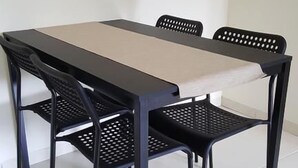 Een eettafel met twee stoelen, een lichtkleurige tafelkleed en zwarte metalen stoelen met geperforeerde rugleuningen.