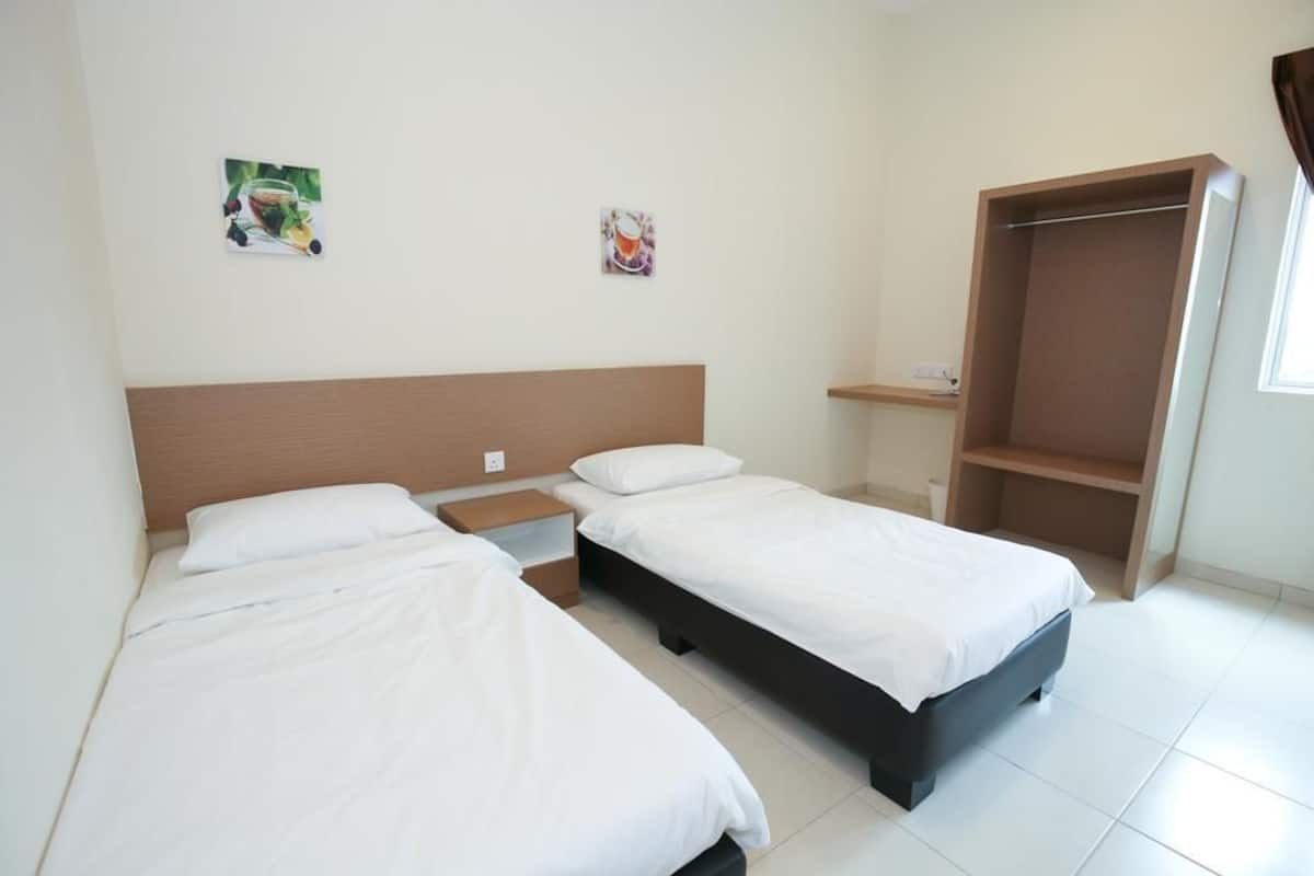Une chambre d’hôtel avec deux lits simples, une tête de lit en bois, une petite table de chevet, une étagère et une armoire.