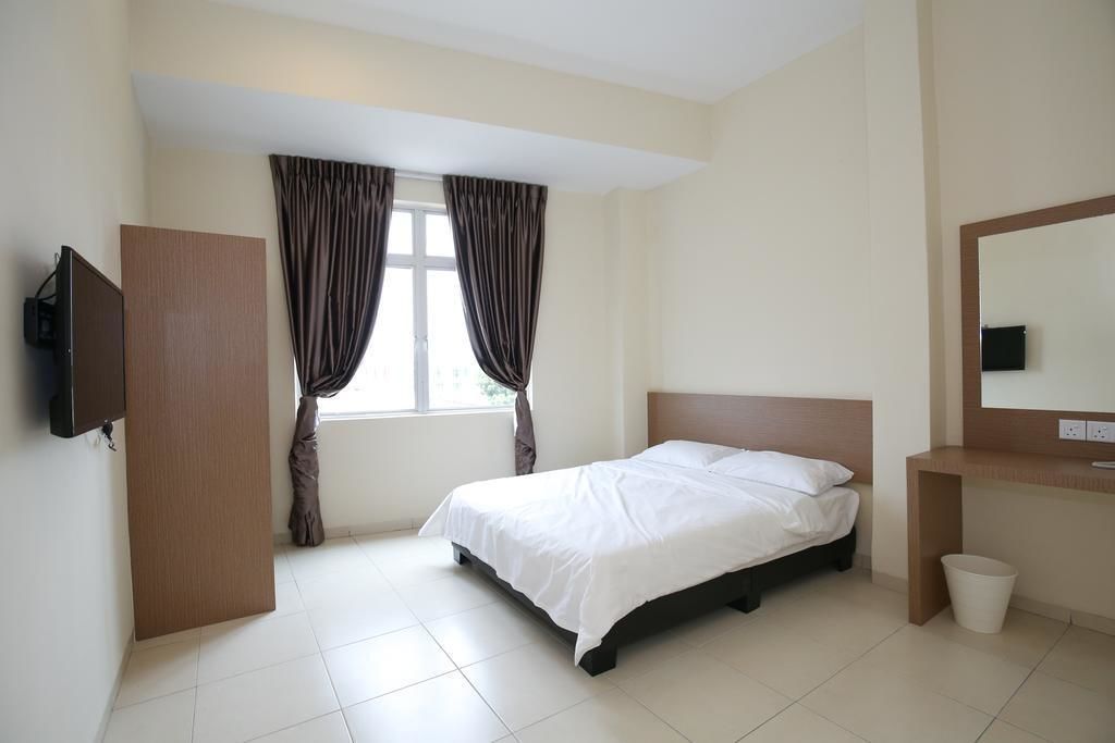 A hotel room with a bed, a TV mounted on the wall, a window with curtains, and a small bedside table.