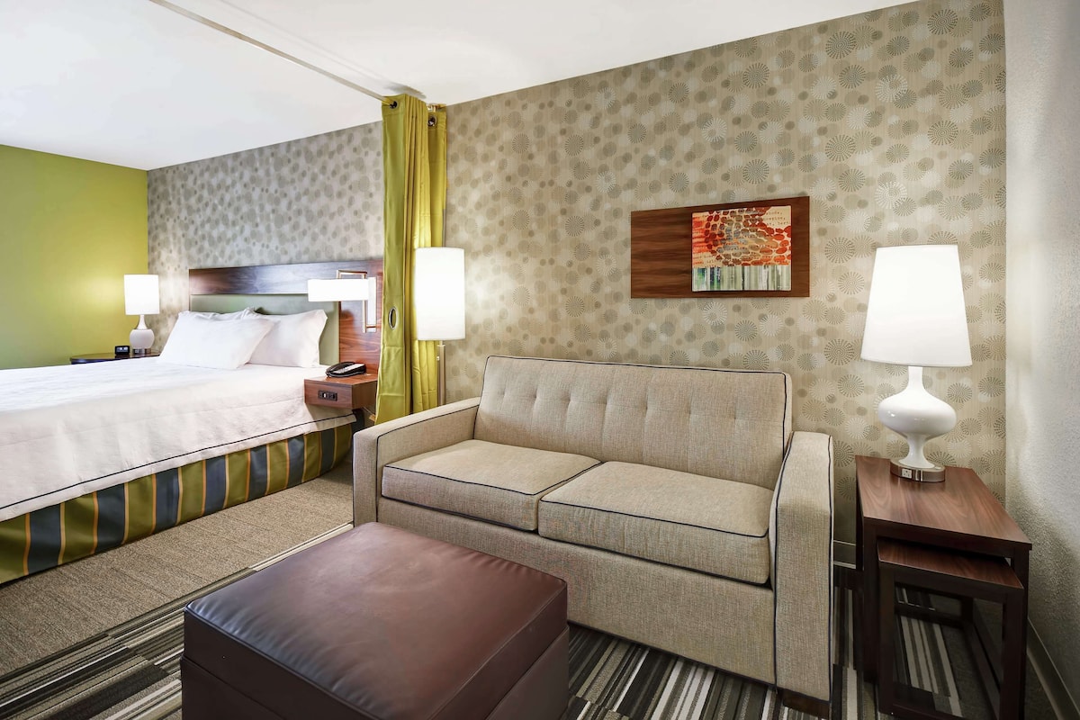 A hotel room with a bed, a sofa, a coffee table, and two bedside tables with lamps.