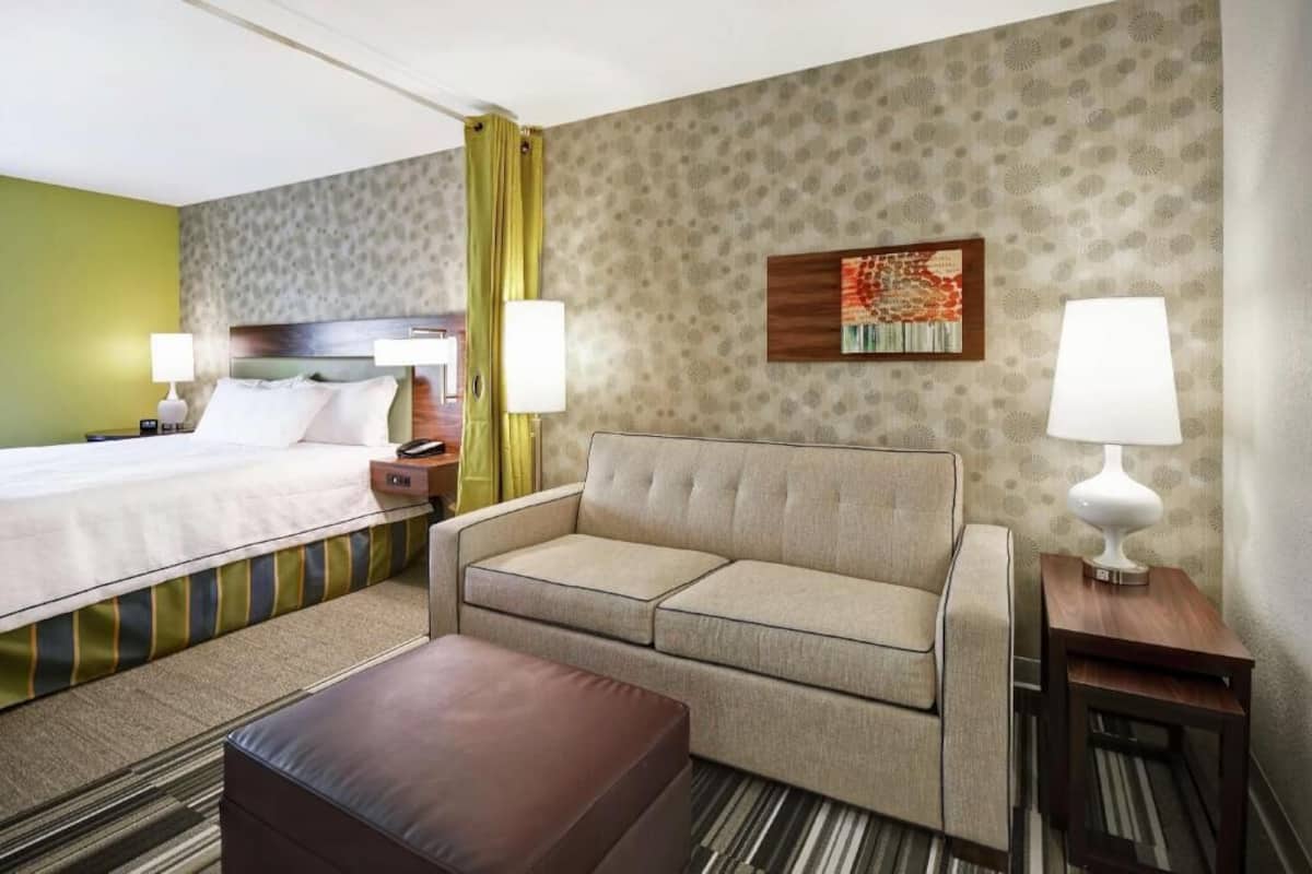 A hotel room with a bed, a sofa, a small table, and a lamp.