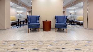 Un hall de hotel con dos sillones azules, una mesita de madera y una alfombra beige con diseño azul.