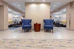 Un hall de hotel con dos sillones azules, una mesita de madera y una alfombra beige con diseño azul.