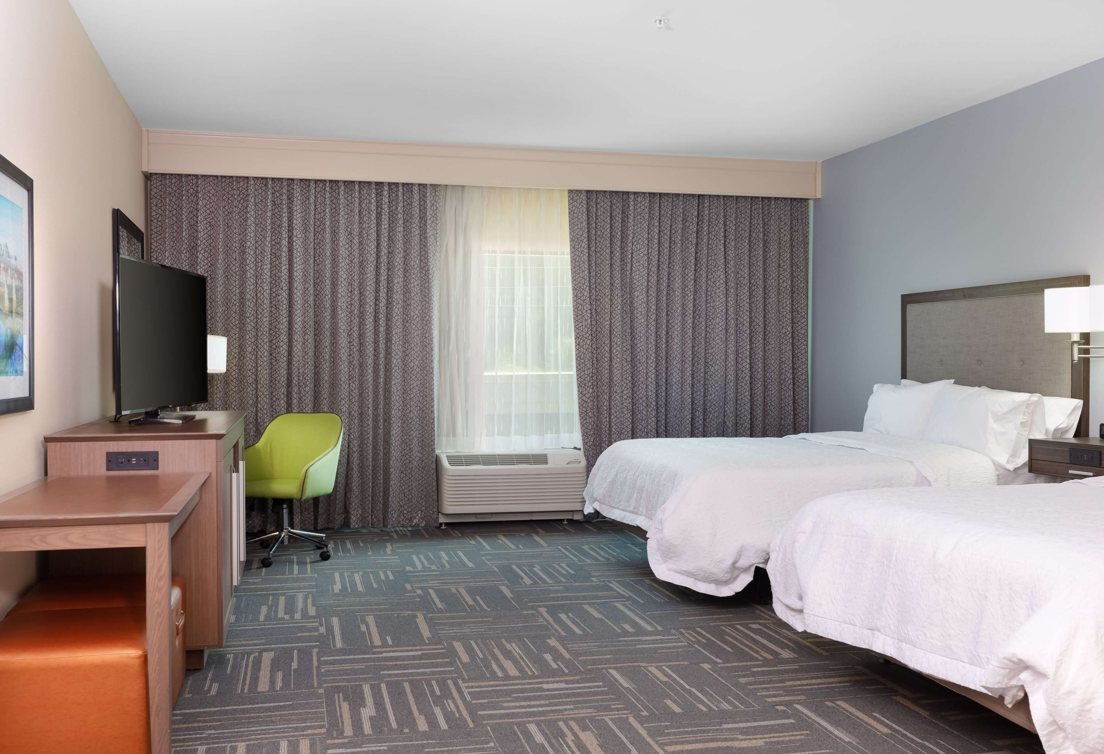 A hotel room with two beds, a desk, a chair, a television, and a window with curtains.