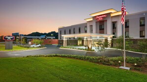 A Hampton Inn hotel with a well-lit entrance, a parking lot, and a landscaped area with trees.