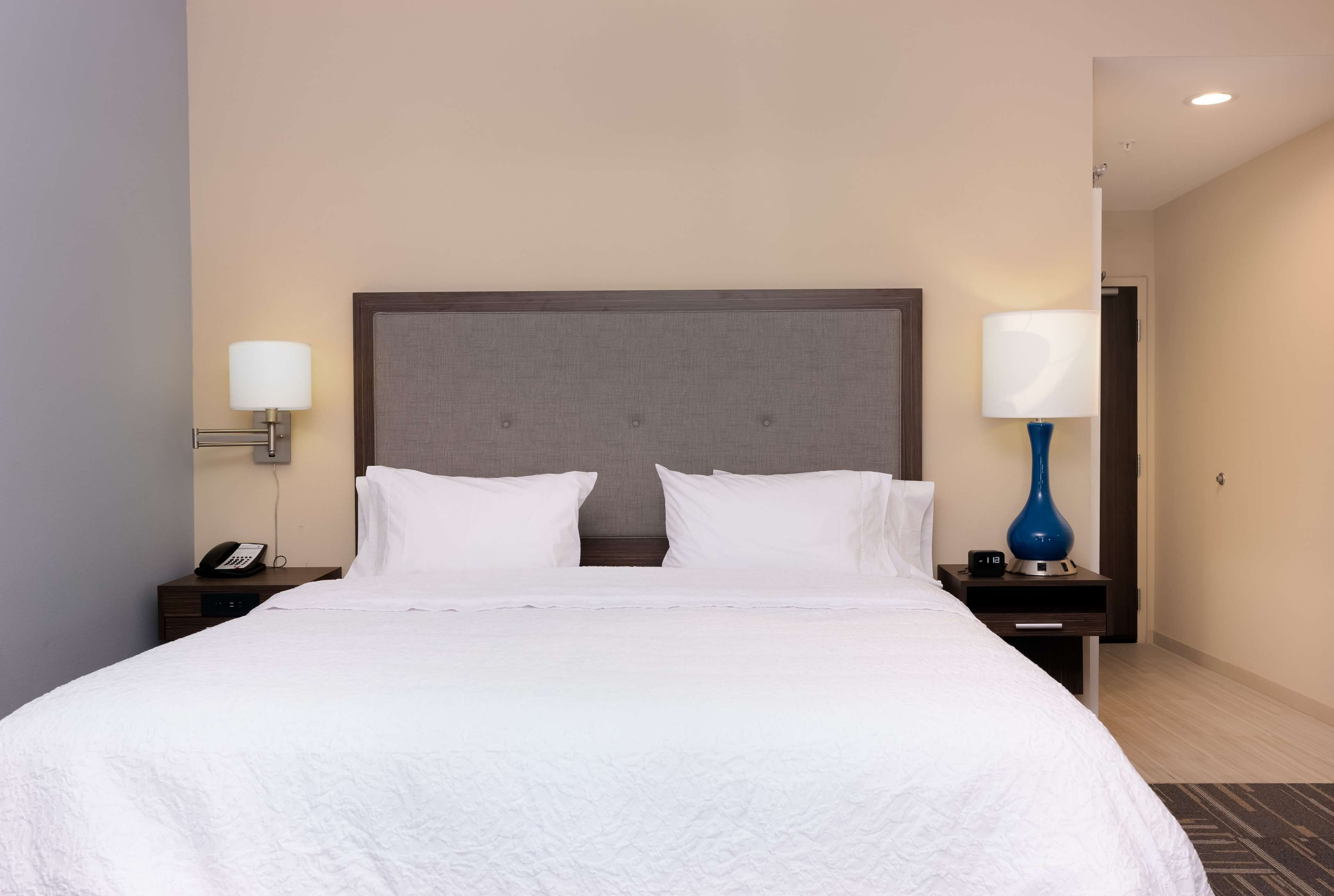 A neatly made bed with white linens, two bedside tables with lamps, and a plain wall.