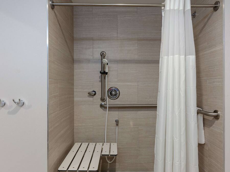 A shower with a handheld showerhead, a handheld shower attachment, and a towel rack.