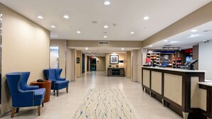 Vestíbulo de hotel con recepción, zona de estar y pasillo que conduce a los ascensores.