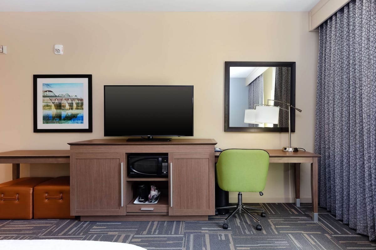 A hotel room with a flat-screen TV, a desk with a chair, a microwave, a small cabinet, and a large mirror.