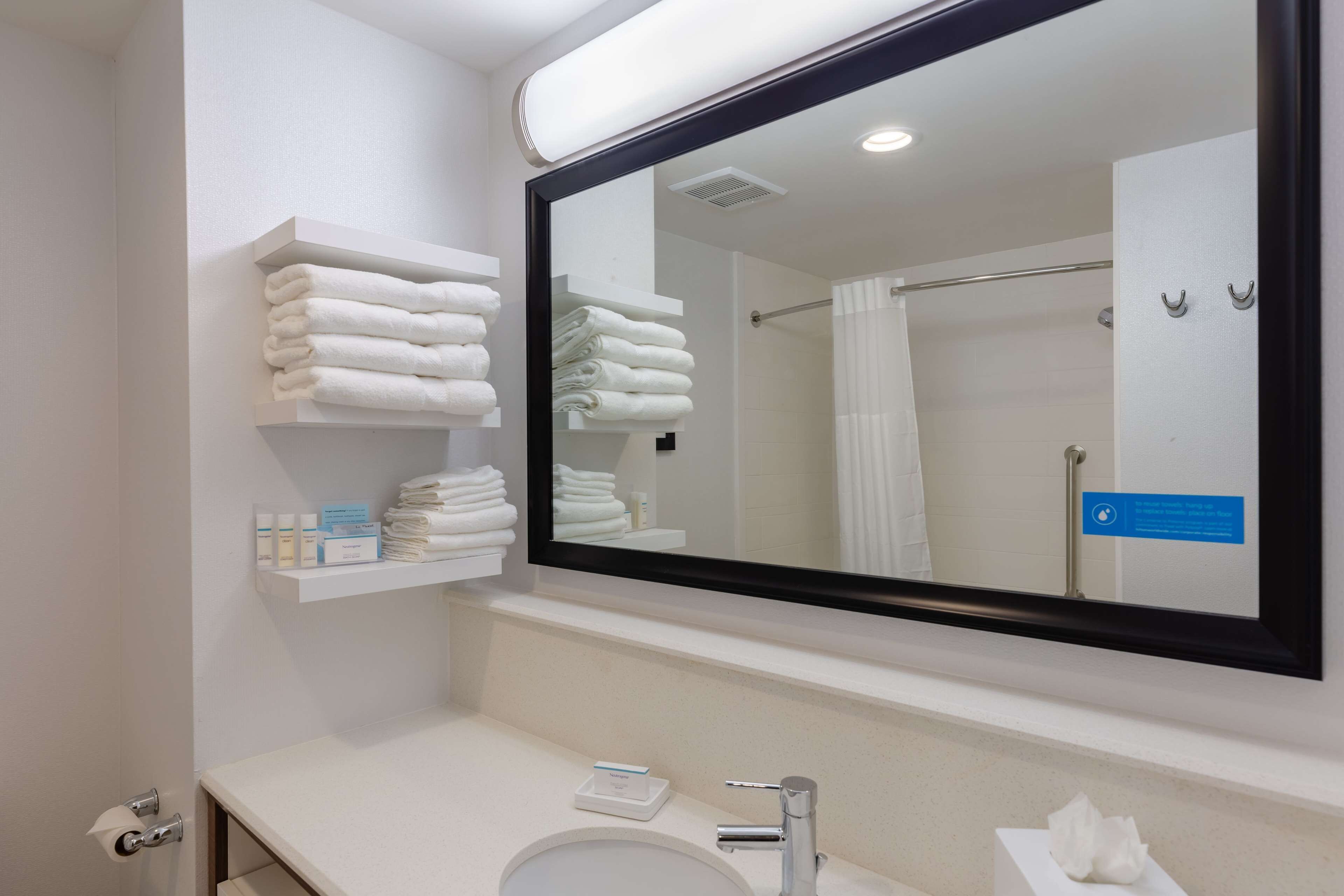 Une salle de bain moderne avec un grand miroir, un lavabo et des étagères où sont rangées les serviettes et les articles de toilette.