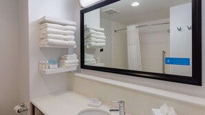 A modern bathroom with a large mirror, a sink, and shelves holding towels and toiletries.