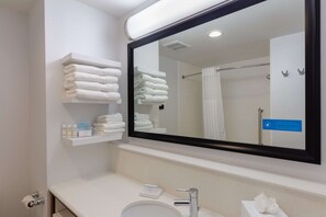A modern bathroom with a large mirror, a sink, and shelves holding towels and toiletries.