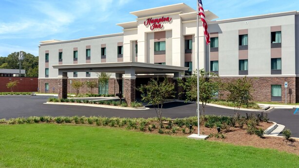 A Hampton Inn hotel with a modern facade, a covered entrance, and a landscaped parking area.