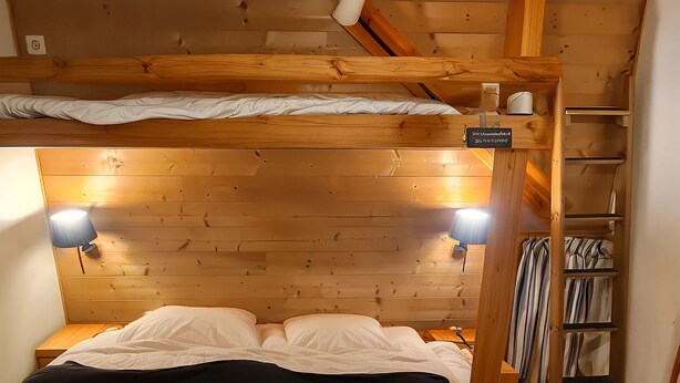 A wooden bunk bed with a headboard, two bedside lamps, and a shelf with striped curtains. - Chalet 1200 (Saint-François-Longchamp)
