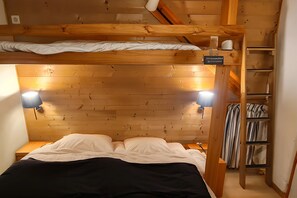A wooden bunk bed with a headboard, two bedside lamps, and a shelf with striped curtains. - Chalet 1200 (Saint-François-Longchamp)