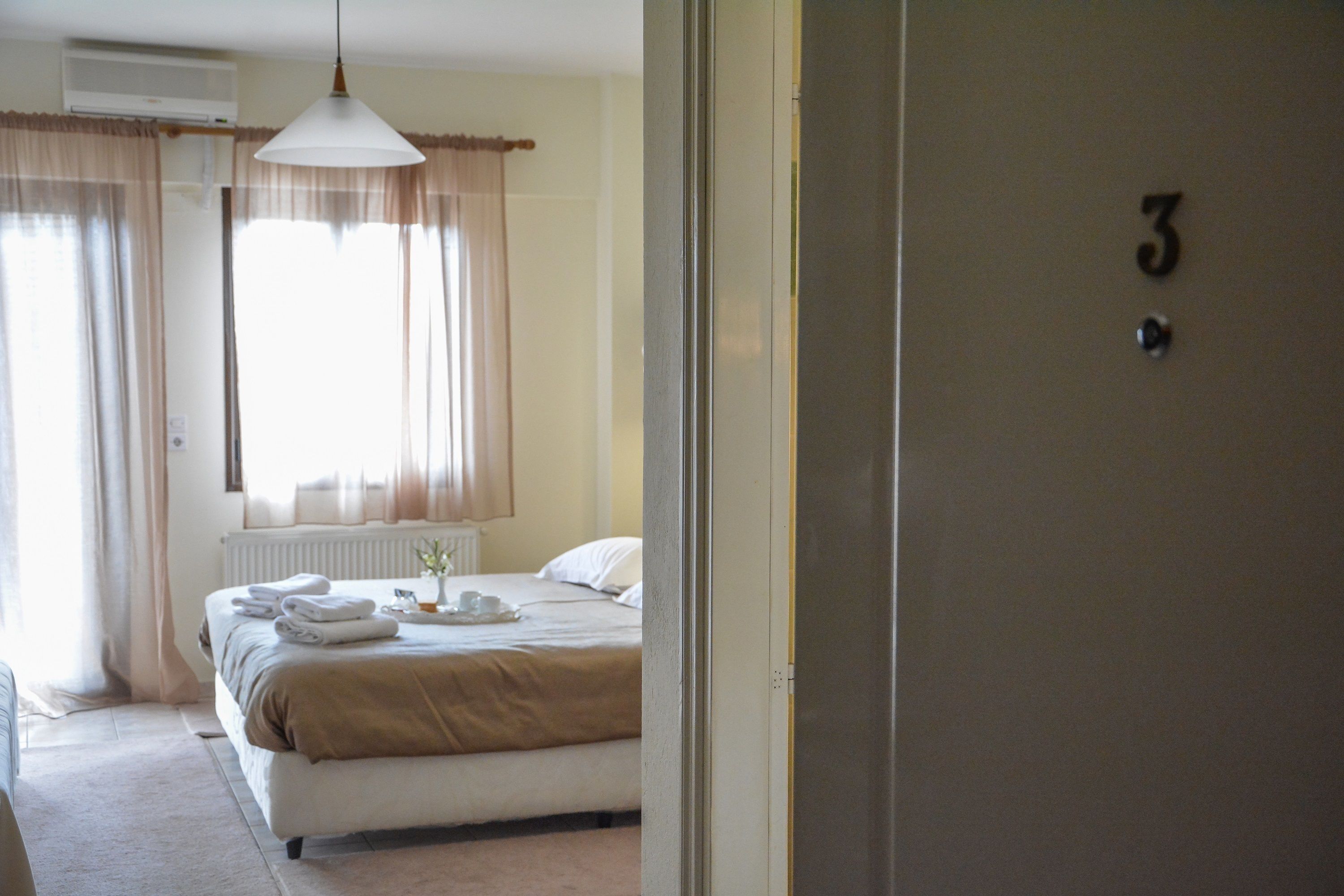 Une chambre d’hôtel avec un lit, un radiateur, une fenêtre avec des rideaux et une porte portant un numéro.