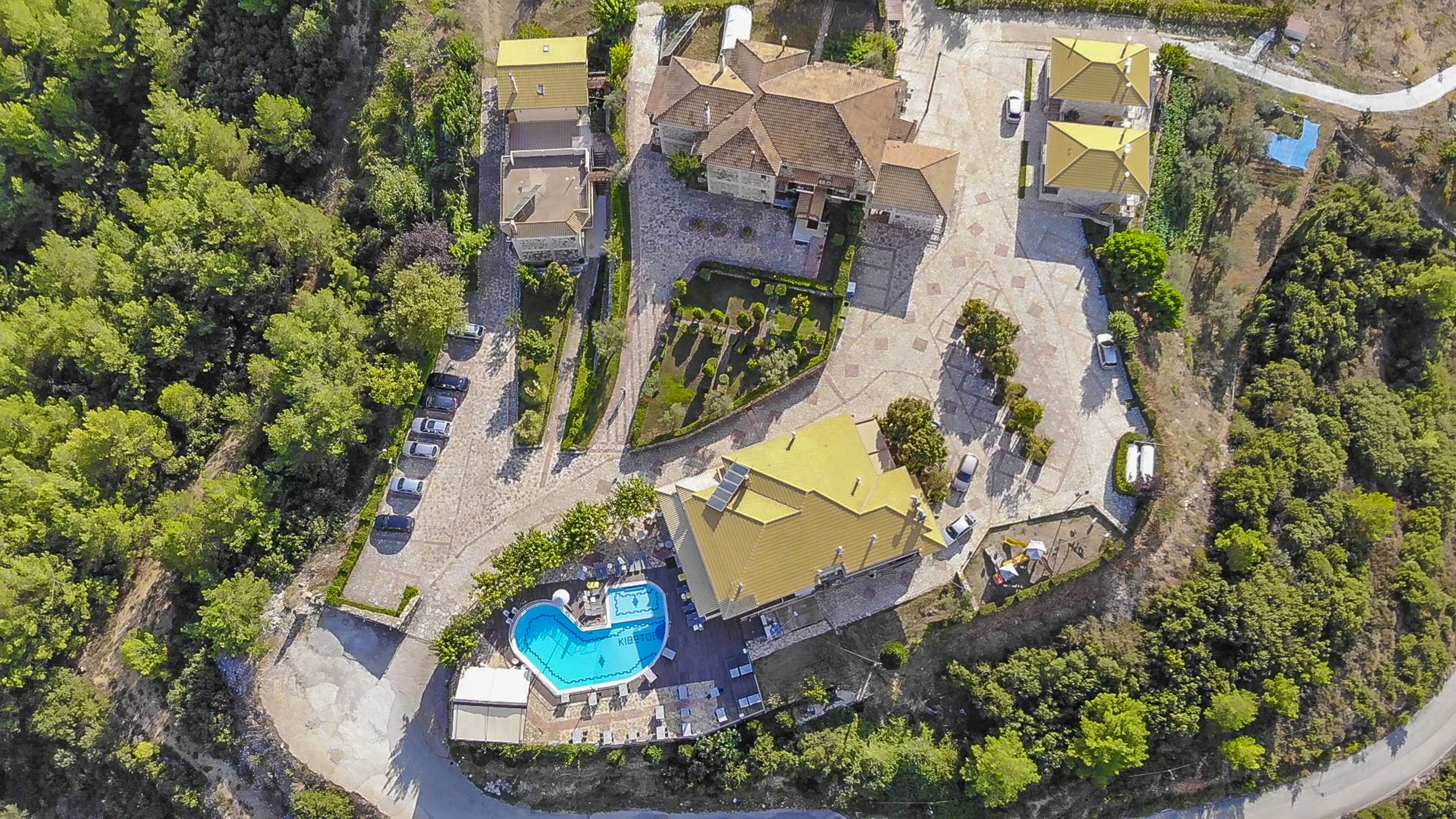 An aerial view of a residential area with a swimming pool, multiple houses, and a winding road.