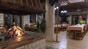 Une cheminée en pierre avec un feu, entourée de tables et de chaises en bois, dans un décor de restaurant.